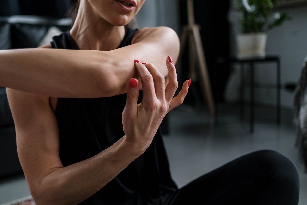 Woman in Black Tank Top Sitting on a Floor Doing Arms Stretching at Home