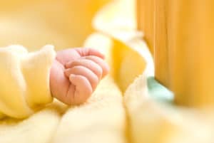 infant hand in baby bed with wooden fence