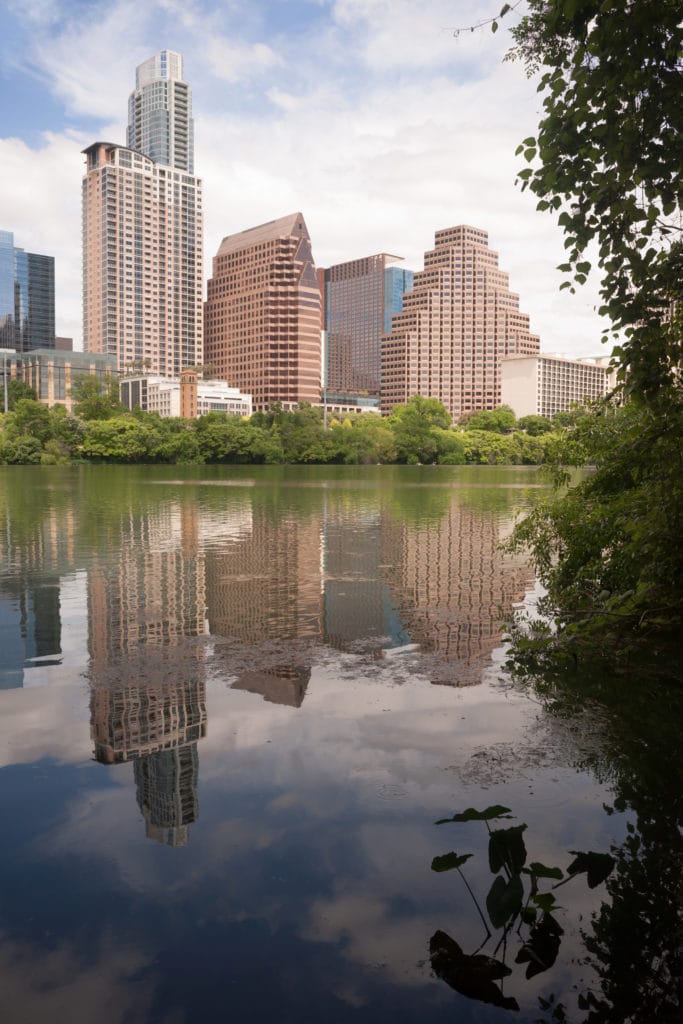 The sun is setting on buildings reflected in the Colorado River as it meanders through Austin, Texas.