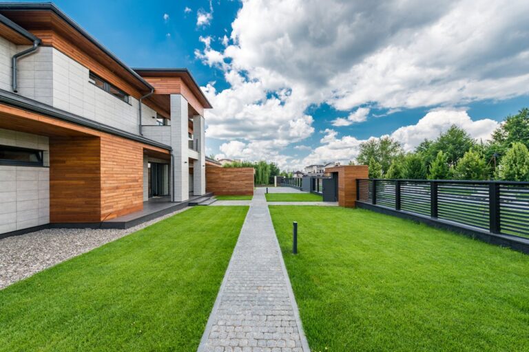 A modern house exterior with contemporary design, lush green lawn, and blue sky offering a tranquil and scenic view.